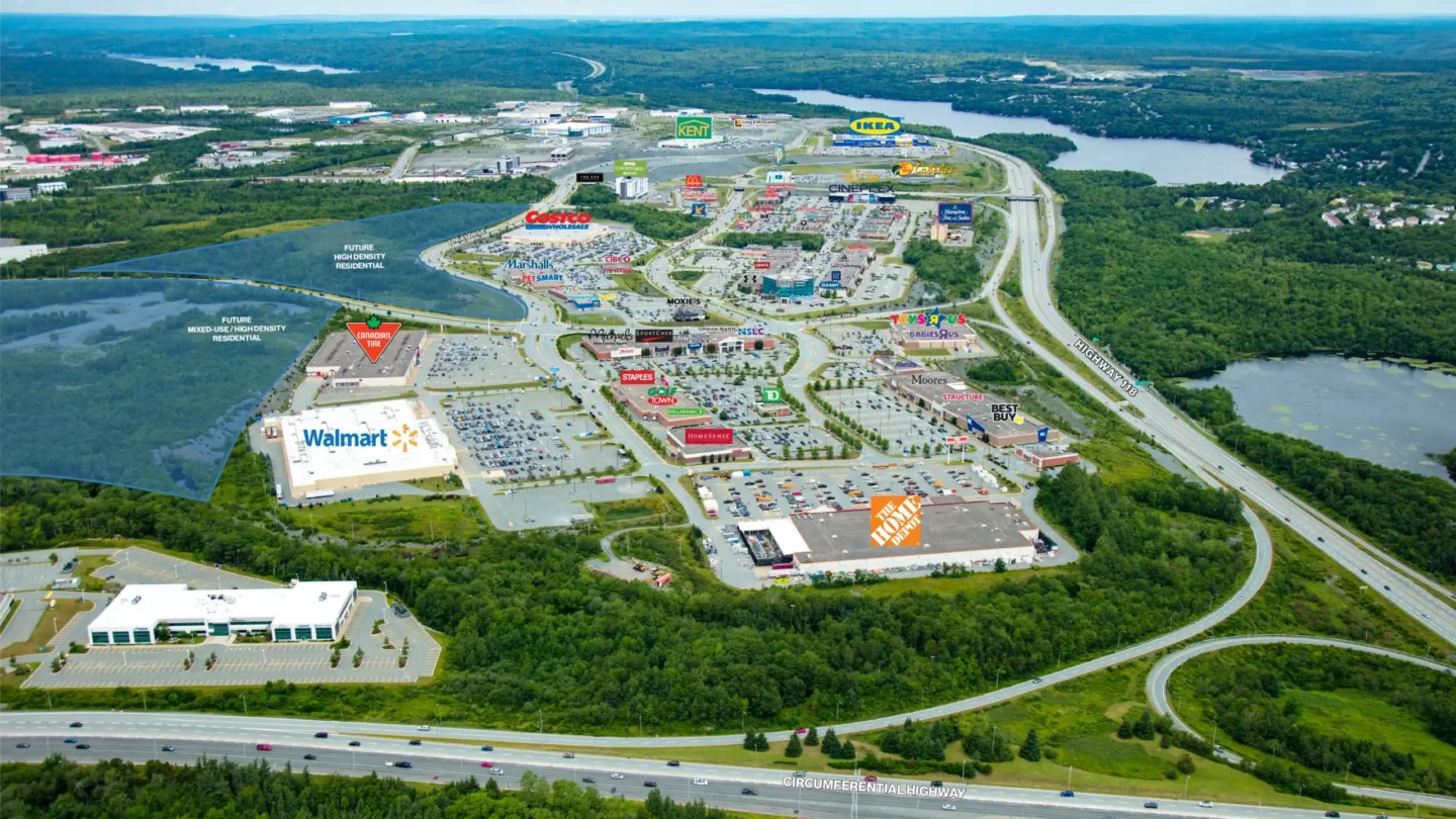 Aerial view of Dartmouth Crossing in Nova Scotia, a large commercial retail district surrounded by forest and lakes. The image shows major anchor stores such as Walmart, Home Depot, IKEA, Costco, Canadian Tire, and Best Buy, all labeled. Other visible brands include Staples, Marshalls, Cineplex, Toys “R” Us, Michaels, HomeSense, and various restaurants like McDonald
