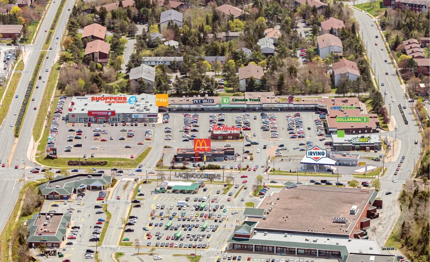 Aerial view of the Clayton Park shopping district in Halifax, Nova Scotia. The image shows a large commercial plaza surrounded by residential buildings and tree-lined streets. The main roads visible are Dunbrack Street on the left and Lacewood Drive running horizontally through the middle of the image. Prominent storefronts include Shoppers Drug Mart, Fit 4 Less, Pet Valu, TD Canada Trust, Pita Pit, Easyhome, Dollarama, Subway, Tim Hortons, and McDonald