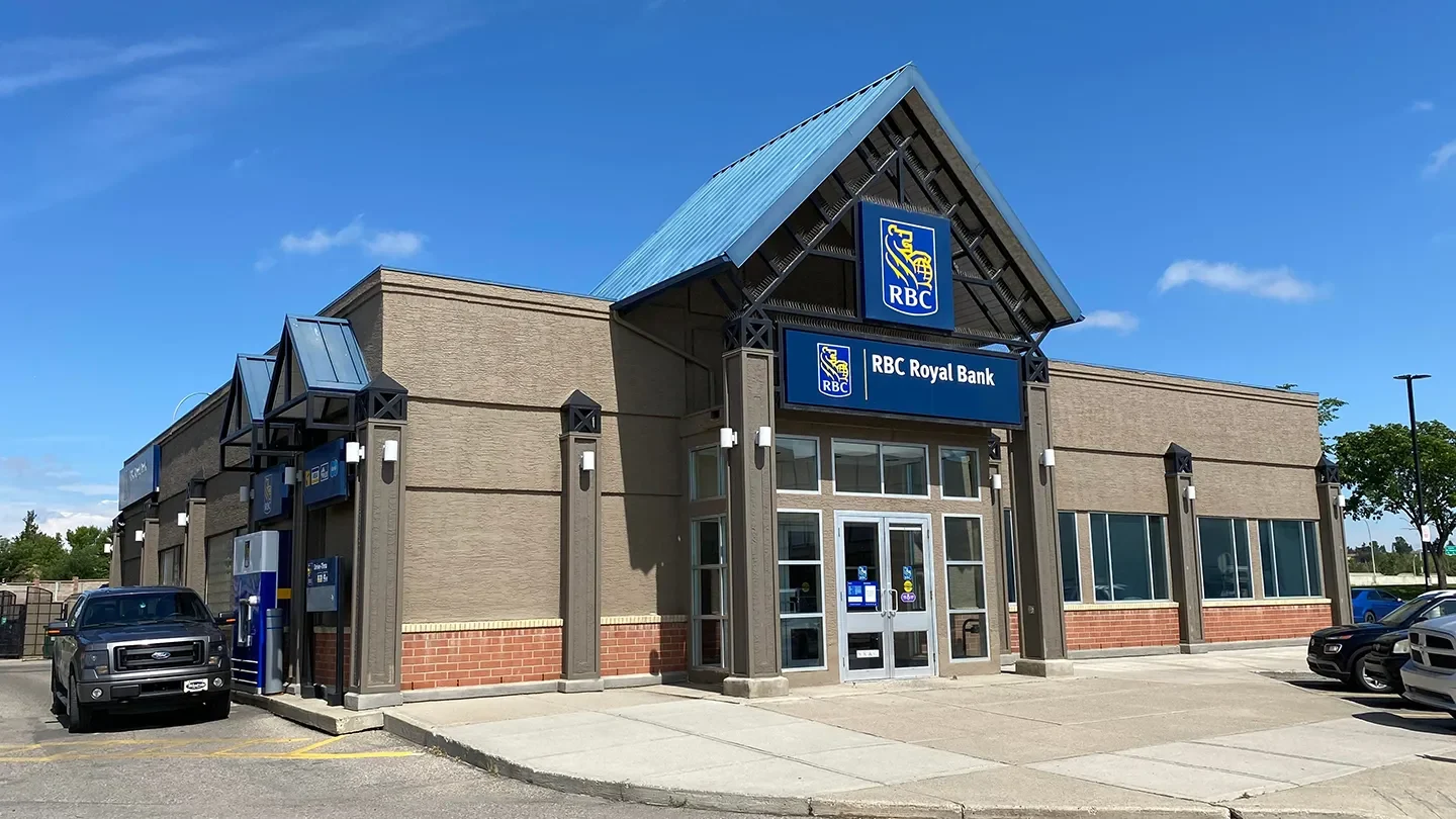 Exterior view of an RBC Royal Bank branch on a clear, sunny day, showing accessible entrances and a drive-thru ATM with a parked truck beside it.