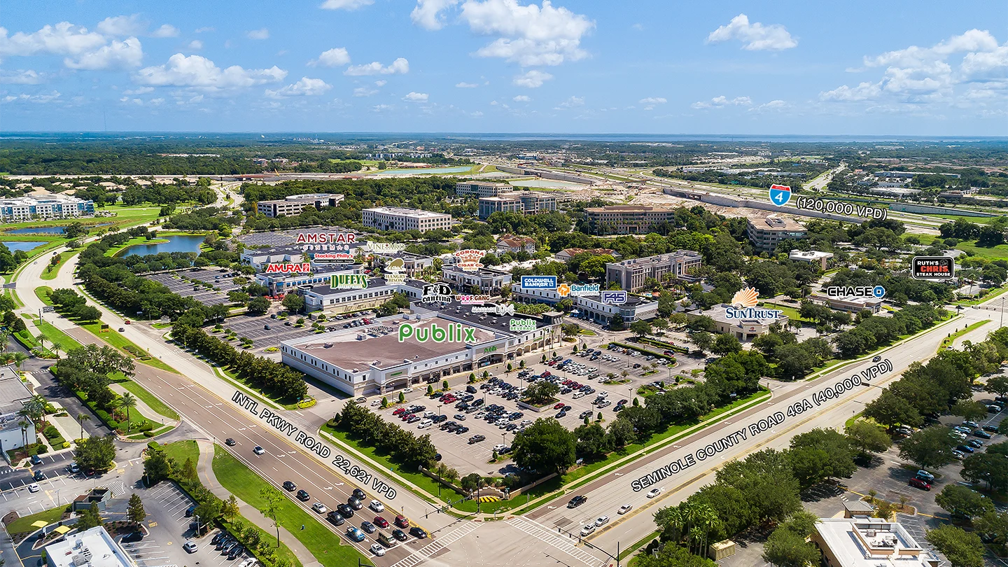 Aerial image of Colonial Town Park with brand labels overlaying tenants such as Publix, AmStar, Chase, Duffy’s, and Ruth’s Chris Steak House, showing parking areas, surrounding roads, and nearby developments.