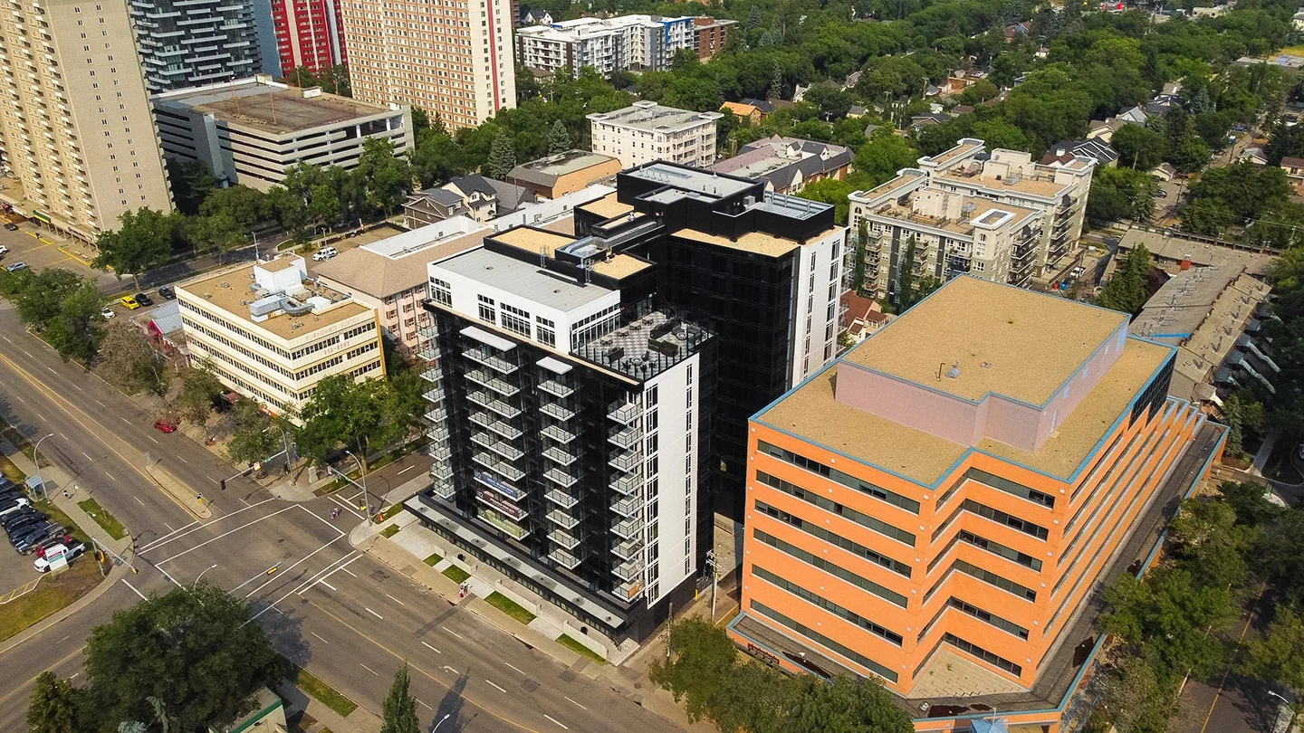 Aerial view of One12 with black and white exterior and balconies, located in an urban neighborhood surrounded by other residential and commercial buildings.