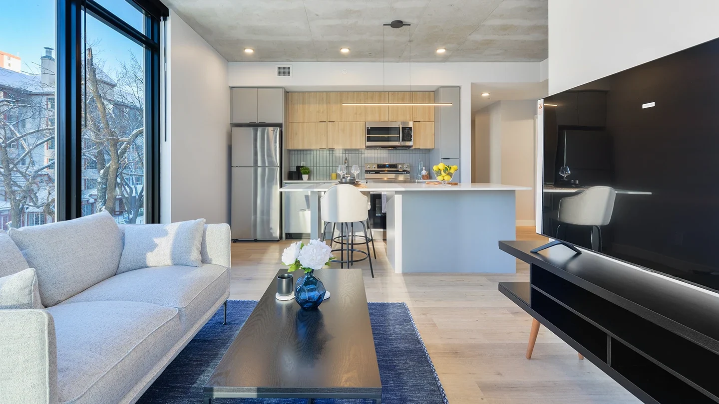 Modern apartment interior featuring an open-concept kitchen with stainless steel appliances, a central island with bar seating, and neutral-toned cabinetry.