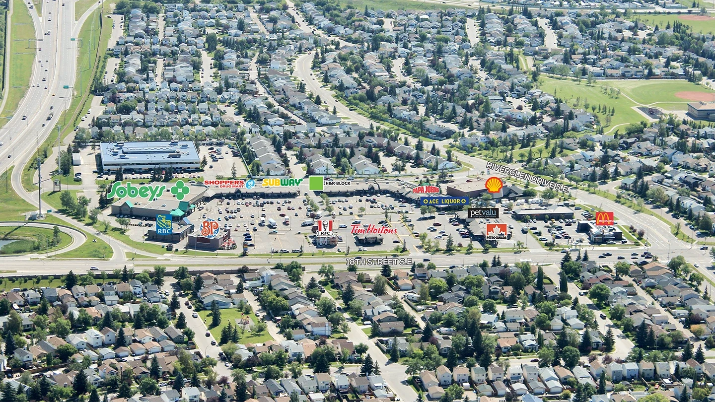 Aerial view of Riverbend Shopping Centre in Calgary, Alberta, highlighting anchor stores like Sobeys, Shoppers Drug Mart, Boston Pizza, and several fast-food restaurants with nearby residential neighborhoods.