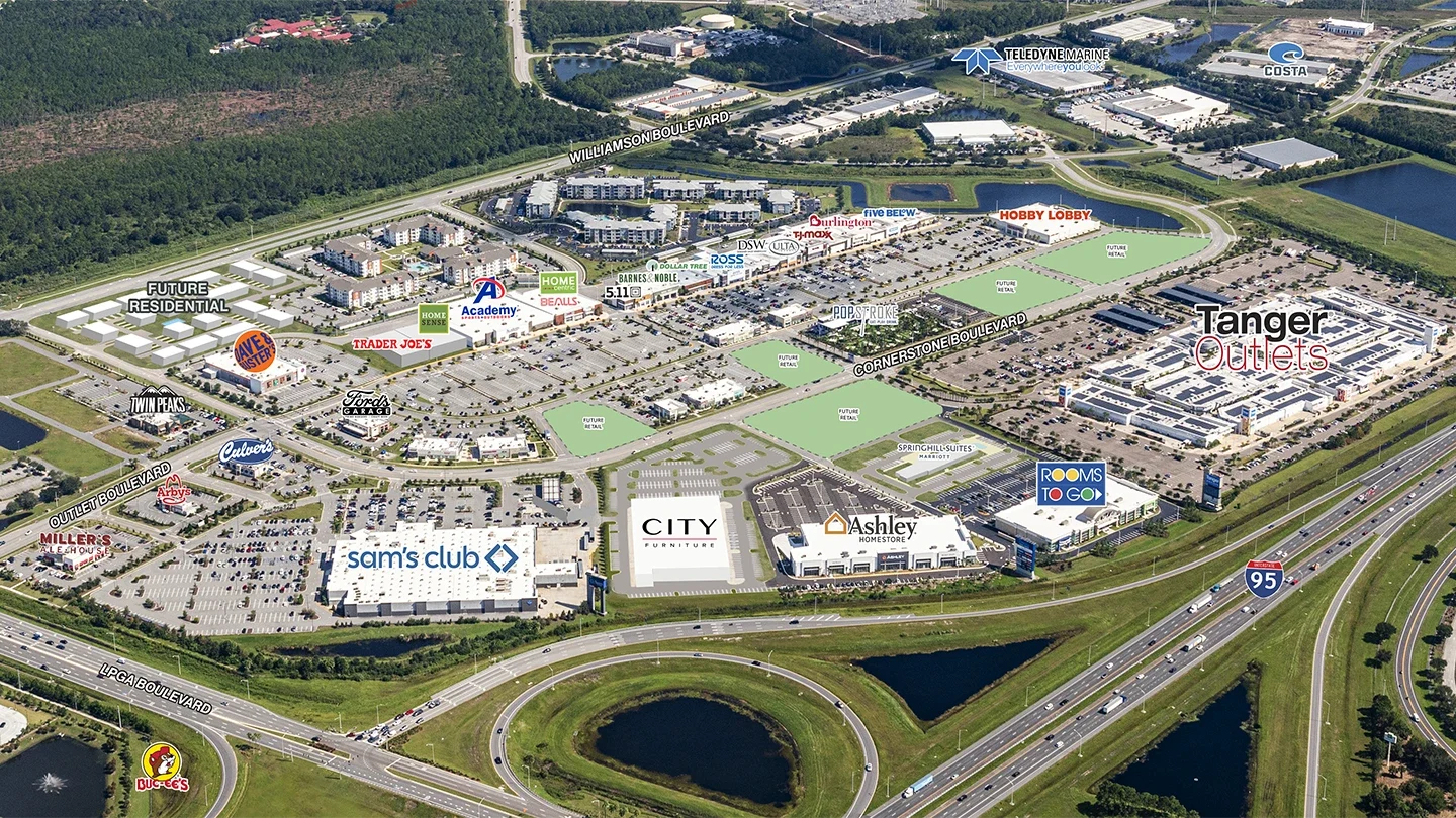 Aerial image of Tomoka Town Center in Daytona Beach, Florida, with major retail stores, restaurants, and future development areas labeled. Key visible businesses include Tanger Outlets, Sam’s Club, Trader Joe’s, Academy Sports + Outdoors, Ashley HomeStore, Rooms To Go, Culver’s, Arby’s, and Buc-ee’s. Streets like LPGA Boulevard, Outlet Boulevard, Williamson Boulevard, and Cornerstone Boulevard are marked. Green spaces are labeled as “Future Retail” and “Future Residential.” The image includes surrounding hotels, water features, and highways, including I-95 in the foreground.