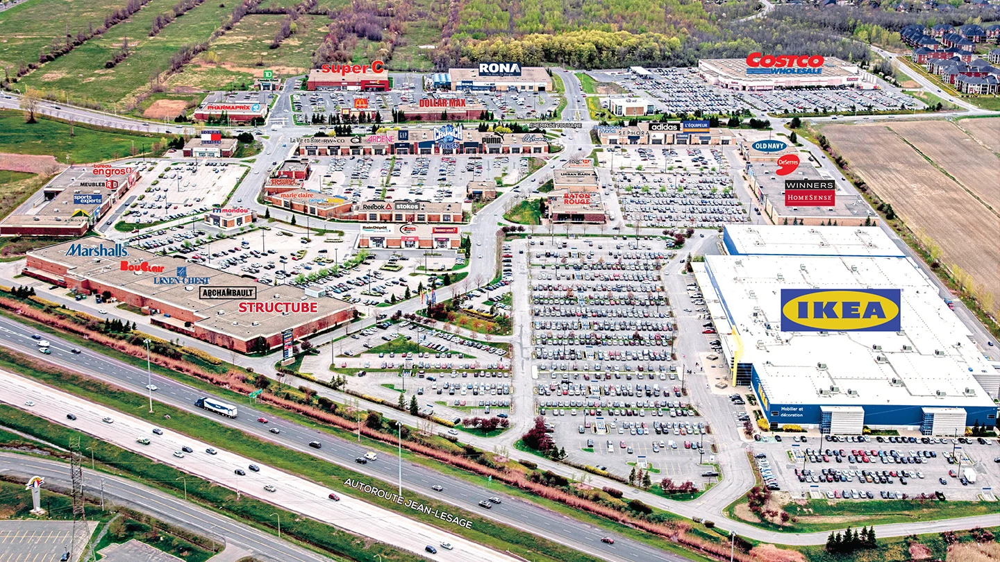 Aerial view of a large commercial shopping district bordered by Autoroute Jean-Lesage. A prominent IKEA store dominates the right side of the image with its large white roof and blue exterior. The complex includes major retailers such as Costco, RONA, Super C, Marshalls, Structube, Winners, HomeSense, and numerous smaller shops and restaurants including Baton Rouge and McDonald