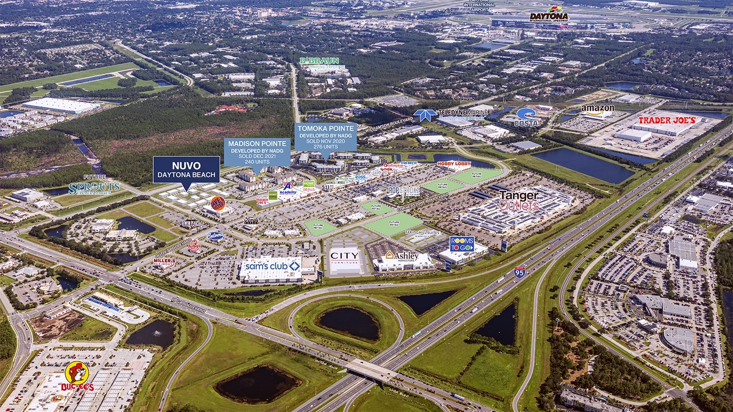 A labeled aerial view of Daytona Beach showing retail and residential developments. Key landmarks such as Trader Joe’s, Amazon, Sam’s Club, Buc-ee’s, and Tanger Outlets are marked. Two residential communities—Madison Pointe and Tomoka Pointe—are labeled along with the NUVO Daytona Beach development site. Major highways, including I-95, are visible with looping interchanges and green areas in between.