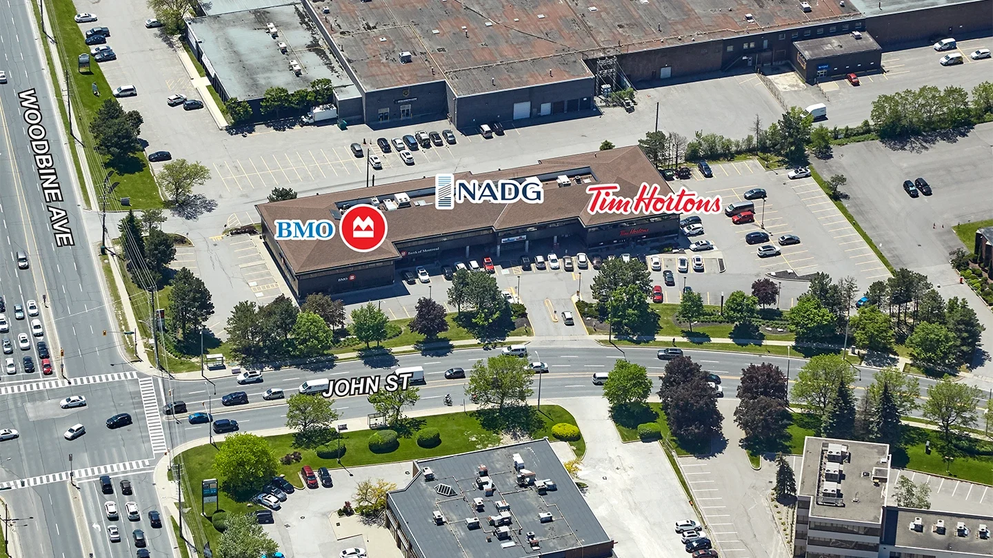 Labeled aerial view of a commercial property at the intersection of Woodbine Avenue and John Street, showing BMO, Tim Hortons, and NADG signage, with adjacent streets and nearby buildings visible.