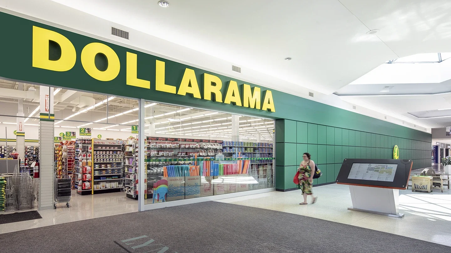 Interior view of the Lynden Park Mall showing the entrance to a brightly lit Dollarama store. A person is walking past the storefront, and a digital mall directory is positioned in the hallway outside.