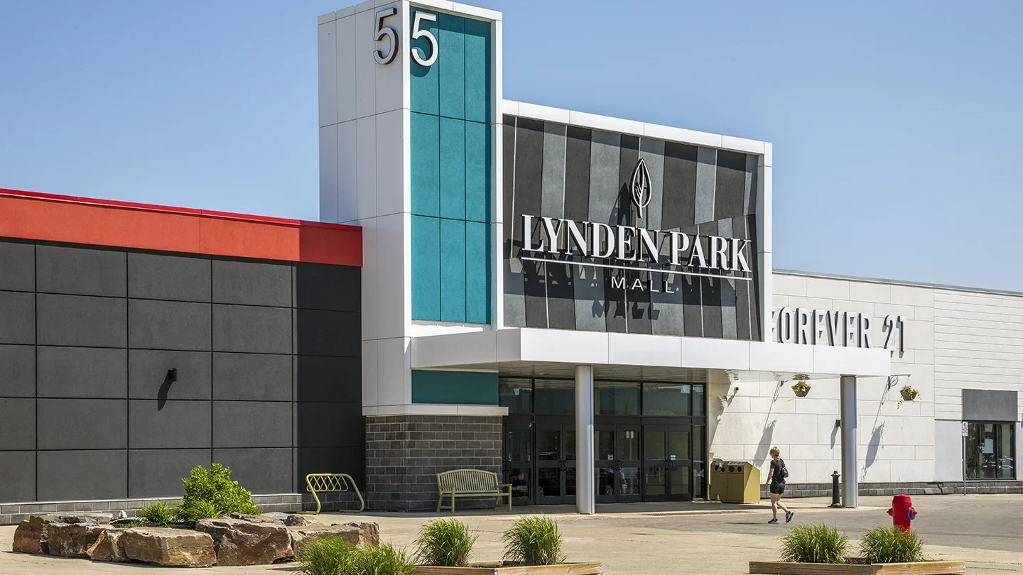 Exterior view of the Lynden Park Mall entrance marked with the number 55. The entrance features modern architectural elements with red, teal, and black accents. A Forever 21 store is visible on the right, with a pedestrian walking toward the entrance.
