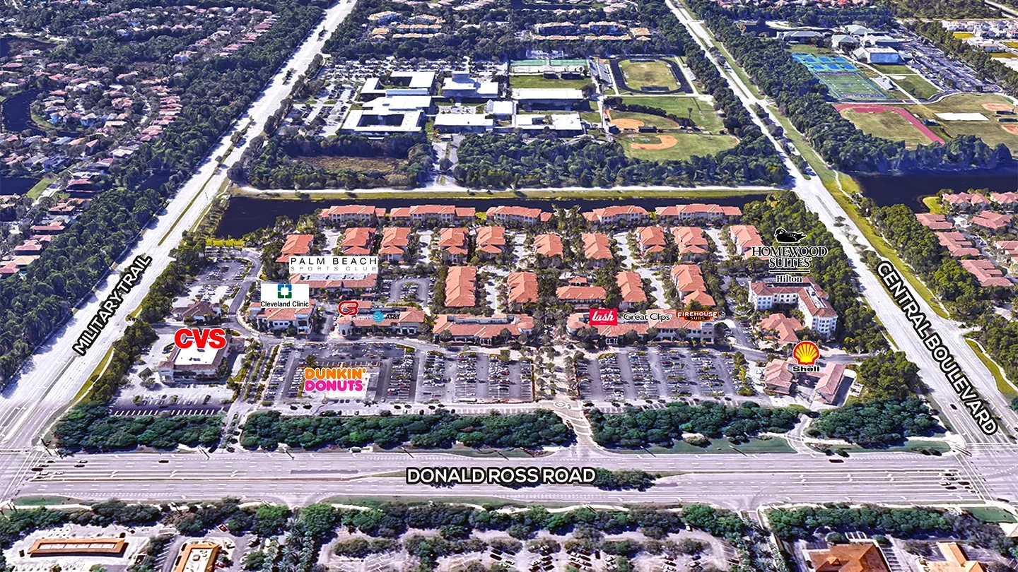 High-angle aerial view labeled image of Donald Ross Village showing store names including CVS, Dunkin’ Donuts, Palm Beach Sports Club, and Shell. The plaza is bordered by Donald Ross Road, Military Trail, and Central Boulevard.