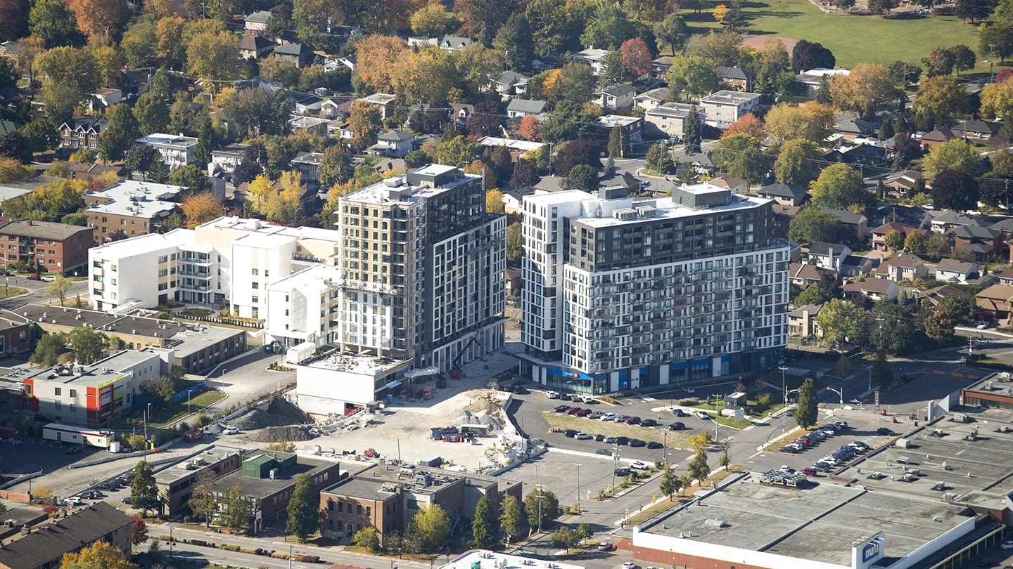 Aerial view of modern mid-rise buildings surrounded by houses, parking lots, and autumn trees.
