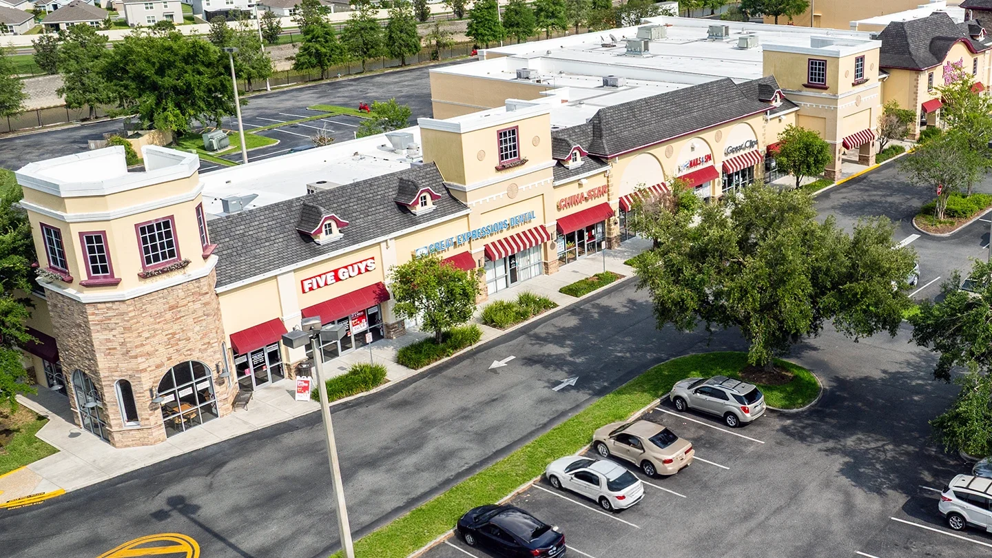 Elevated view of a retail strip at Zephyr Commons with storefronts including Five Guys, Great Expressions Dental, China Star, and Great Clips. Red awnings line the walkway, and trees fill the foreground parking lot.
