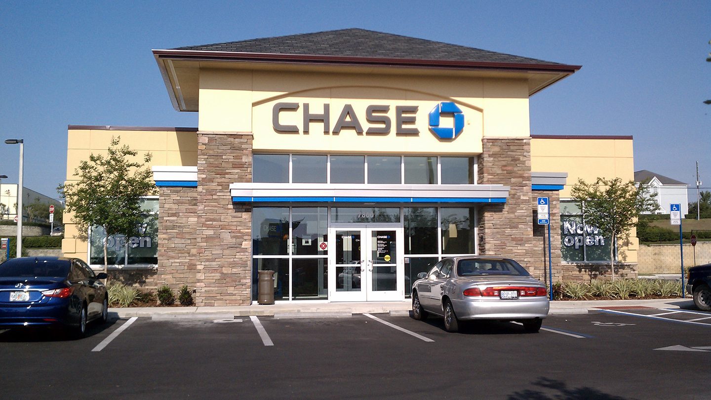 Frontal view of a Chase Bank branch at Zephyr Commons, with a stone facade and bold signage above a glass door entrance, flanked by parked cars.