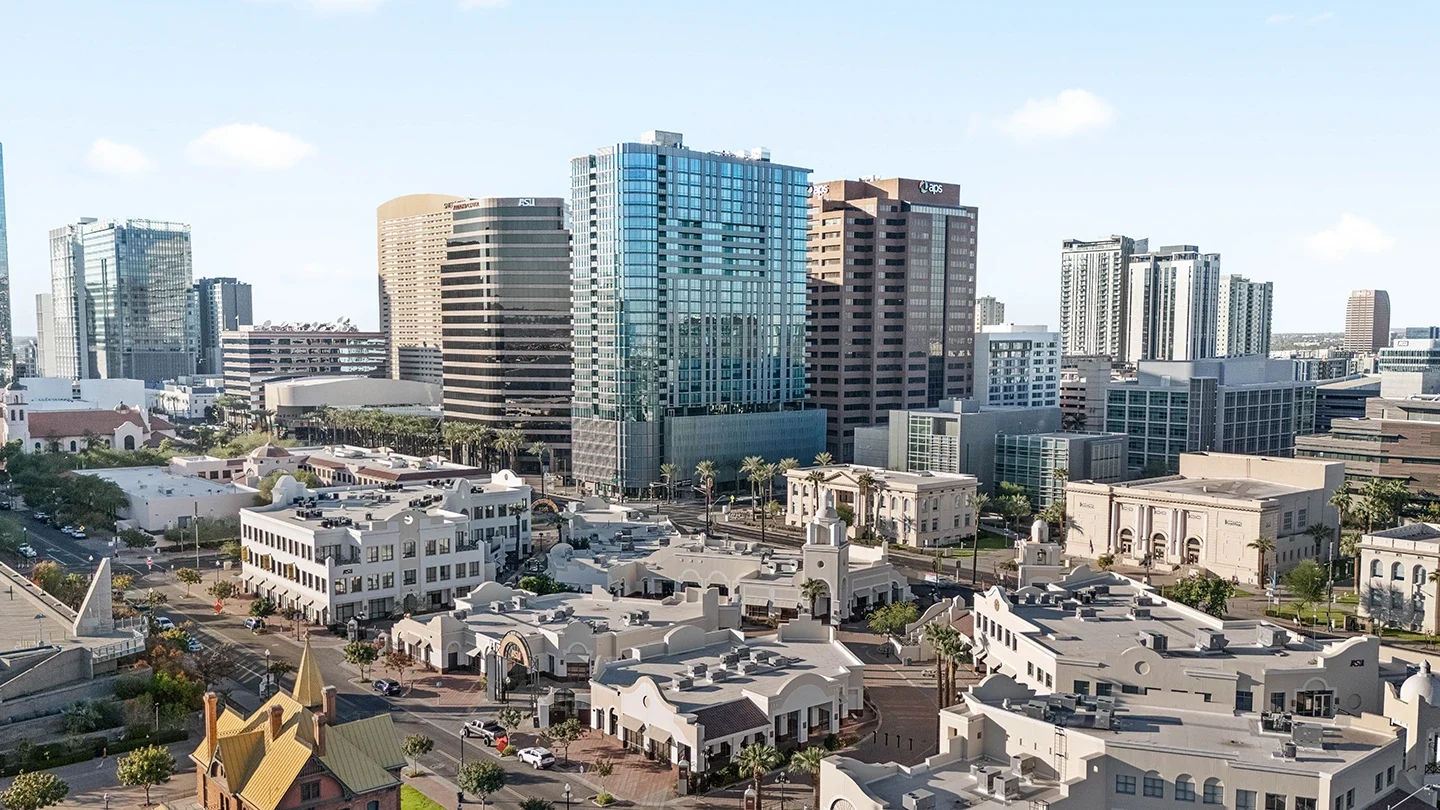 Daytime aerial view of a modern glass high-rise surrounded by mid-rise office towers and historic low-rise buildings, highlighting the contrast between old and new architecture in a downtown urban setting.